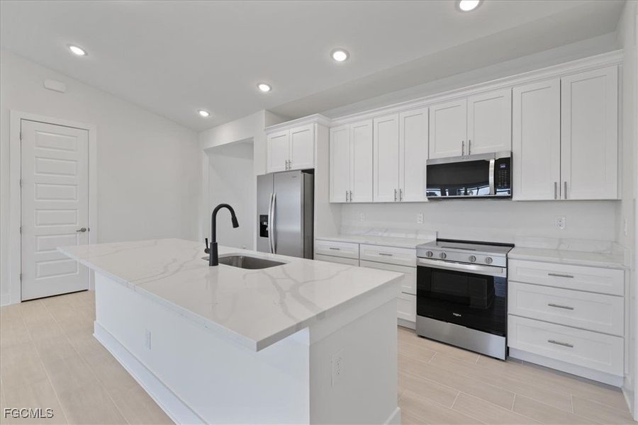 Kitchen with appliances with stainless steel finishes, white cabinets, light stone countertops, recessed lighting, and a center island with sink