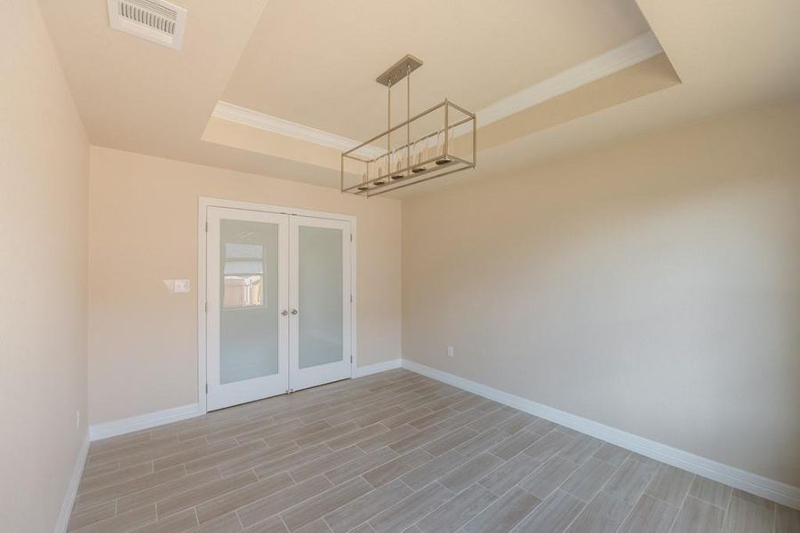 Spare room with french doors, a raised ceiling, crown molding, and wood finish floors Spare room with french doors, a raised ceiling, crown molding, and wood finish floors