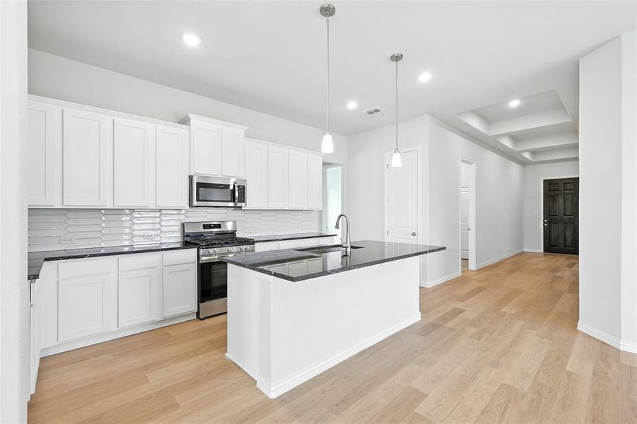 Kitchen featuring stainless steel appliances, a kitchen island with sink, white cabinetry, light wood finished floors, and pendant lighting Kitchen featuring stainless steel appliances, a kitchen island with sink, white cabinetry, light wood finished floors, and pendant lighting