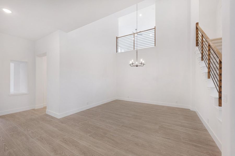 Open living area with high ceilings, chandelier, wood floors, and staircase with metal railing