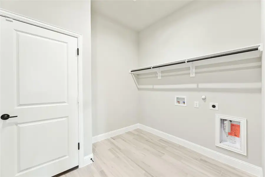 Laundry room with wall-mounted shelf, hanging rod, washer hookups, and light wood-look floors Laundry room with wall-mounted shelf, hanging rod, washer hookups, and light wood-look floors