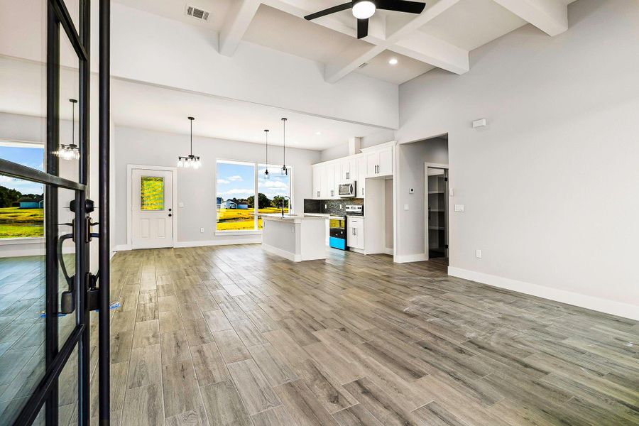This photo showcases a modern, open-concept living space with high ceilings and abundant natural light. The room features light wood flooring, a sleek white kitchen with stainless steel appliances, and large windows offering scenic views. A ceiling fan and stylish pendant lights add to the contemporary feel. This photo showcases a modern, open-concept living space with high ceilings and abundant natural light. The room features light wood flooring, a sleek white kitchen with stainless steel appliances, and large windows offering scenic views. A ceiling fan and stylish pendant lights add to the contemporary feel.
