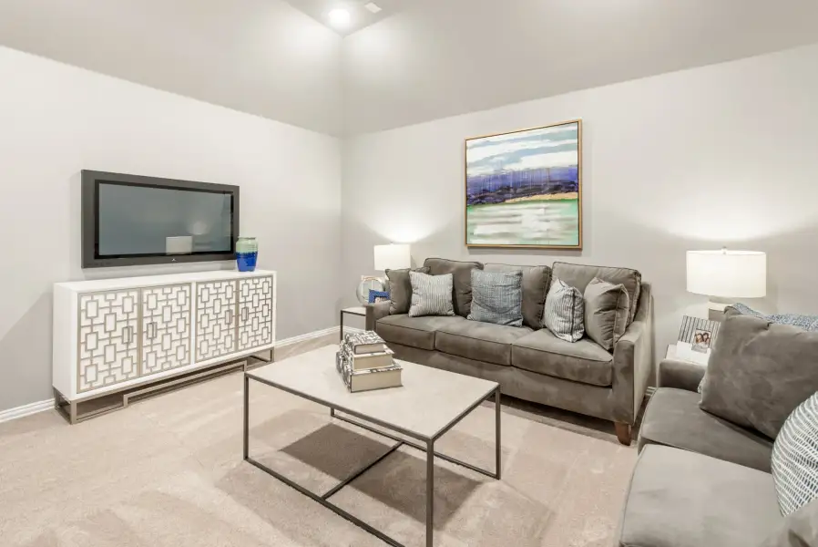 Living room with gray sofa, wall-mounted TV, white media console, and carpeted floors