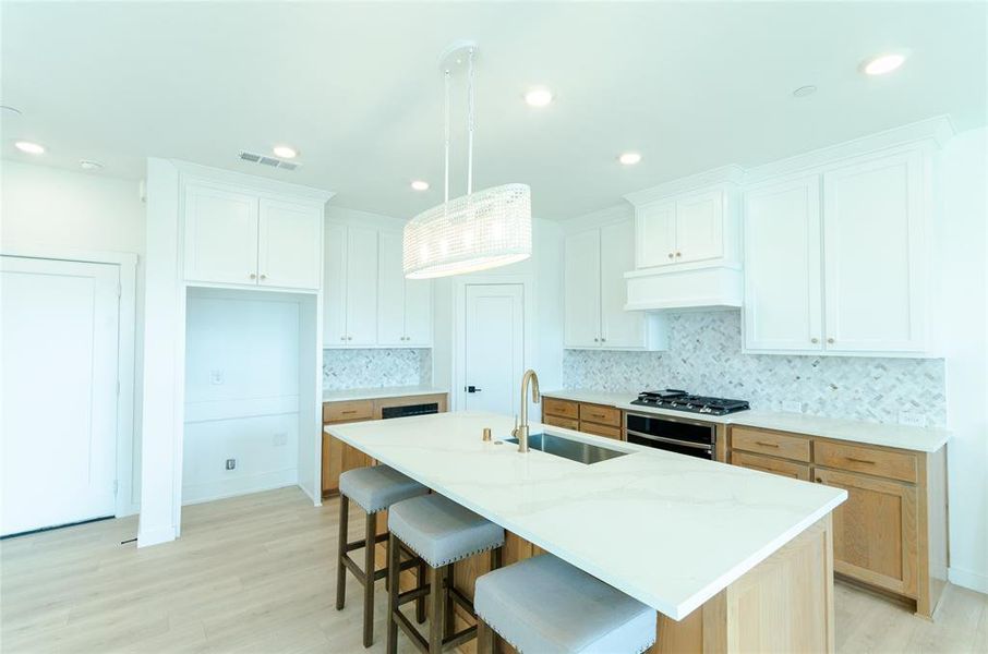 Kitchen featuring a breakfast bar area, appliances with stainless steel finishes, a kitchen island with sink, white cabinetry, and light stone counters