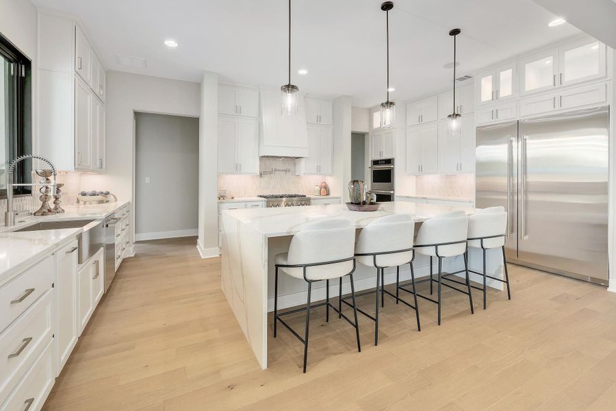 A chef's kitchen features an oversized waterfall island and gleaming stainless steel appliances.