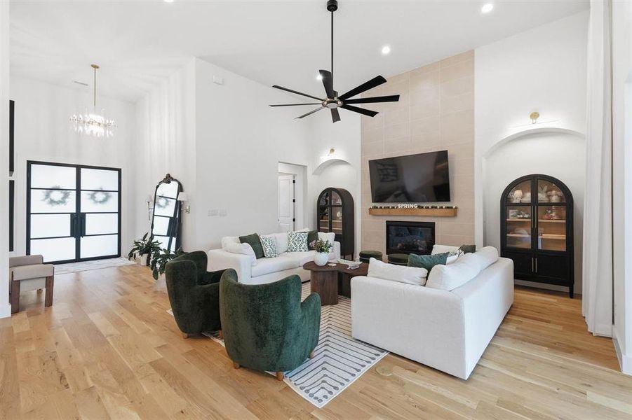 Living room featuring a large fireplace, light wood-style flooring, a ceiling fan, suspended lighting, and lofted ceiling