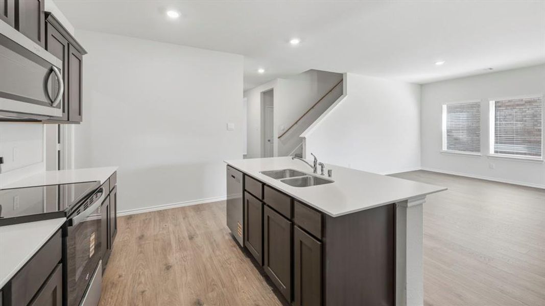 Kitchen featuring stainless steel appliances, light wood finished floors, recessed lighting, dark brown cabinets, and a center island with sink