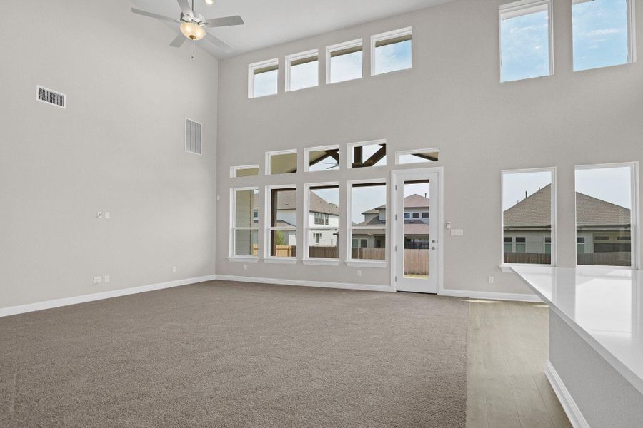 Unfurnished living room featuring a high ceiling, visible vents, a ceiling fan, baseboards, and carpet flooring Unfurnished living room featuring a high ceiling, visible vents, a ceiling fan, baseboards, and carpet flooring