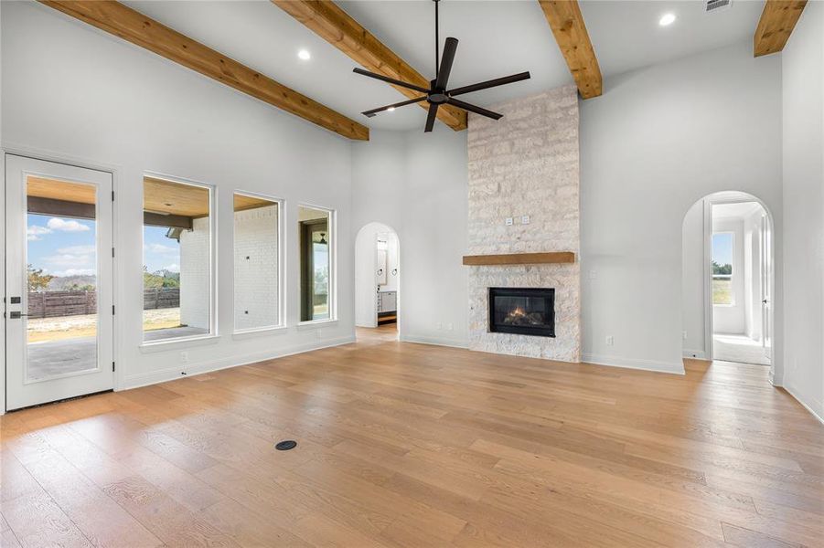 Unfurnished living room featuring arched walkways, a ceiling fan, a stone fireplace, light wood-style floors, and recessed lighting