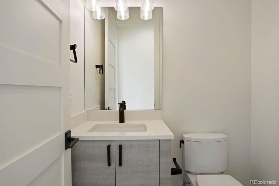 Lower-level powder room with a modern vanity, quartz countertop, black fixtures, and contemporary pendant lighting.