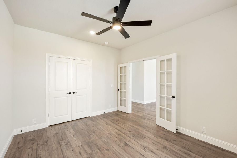 Empty bedroom with hardwood floors, ceiling fan, closet doors, and glass-paned French doors