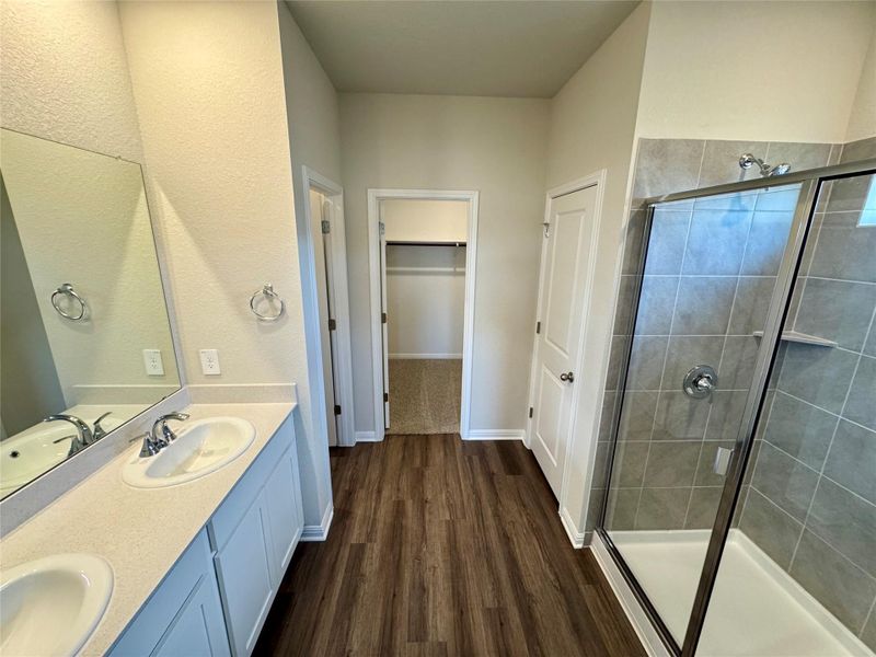 Full bathroom with double vanity, wood finished floors, a shower stall, and a walk in closet Full bathroom with double vanity, wood finished floors, a shower stall, and a walk in closet