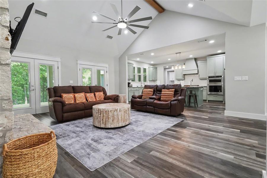 Vaulted ceilings with exposed wood beams, stone fireplace feature, wood-finish flooring, recessed lighting, and a modern ceiling fan