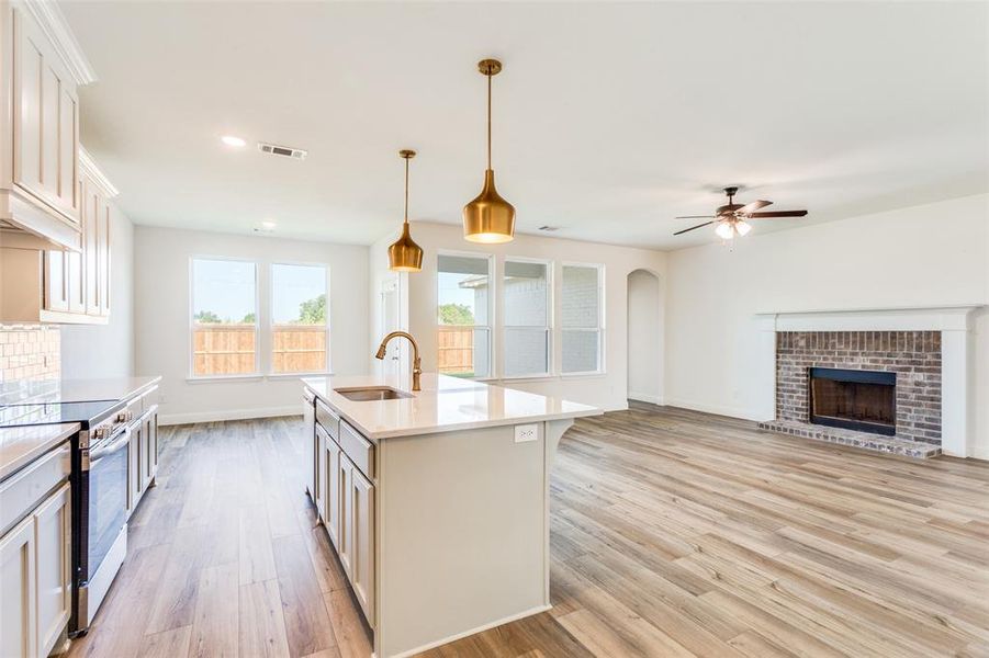 Kitchen with electric range oven, a kitchen island with sink, sink, and light wood-type flooring