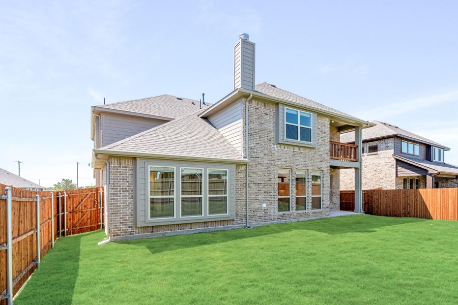 Two-story brick home rear exterior with chimney, second-floor balcony, and fenced backyard with green lawn Two-story brick home rear exterior with chimney, second-floor balcony, and fenced backyard with green lawn