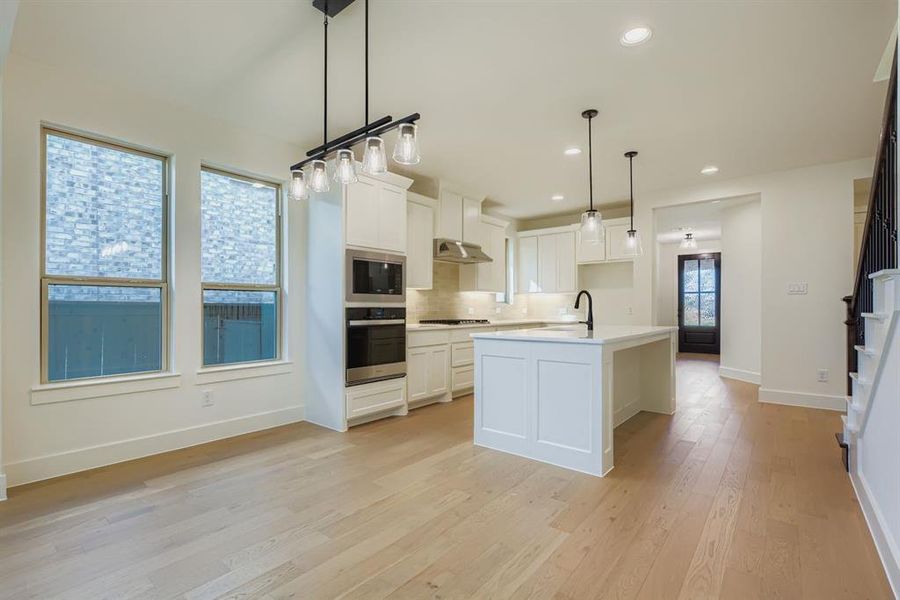 Kitchen featuring tasteful backsplash, white cabinetry, decorative light fixtures, light wood-type flooring, and recessed lighting