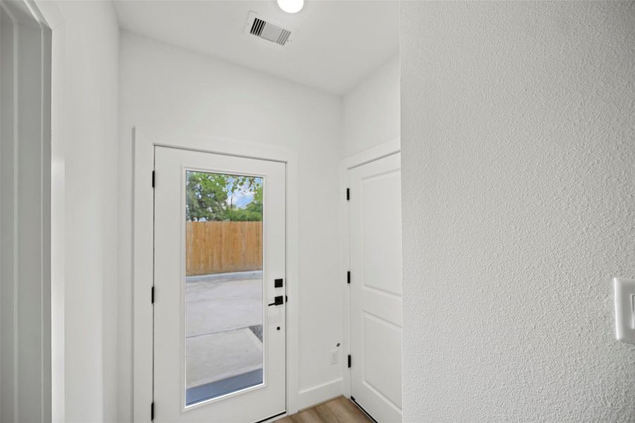 This entryway features a modern glass front door, white walls, and light wood flooring, offering a bright and welcoming atmosphere.