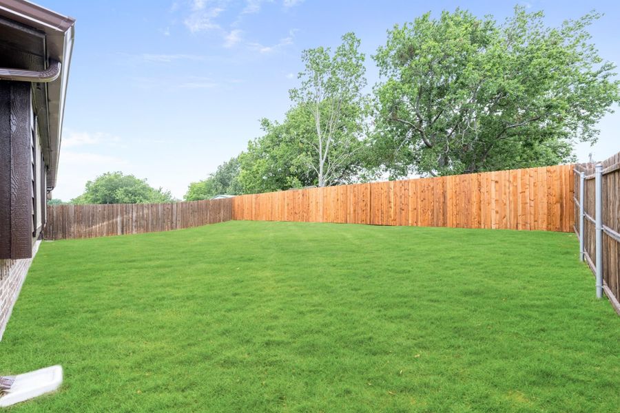 Spacious backyard with green lawn and full wood privacy fence surrounding the yard