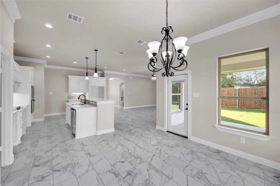 Kitchen featuring pendant lighting, sink, an island with sink, crown molding, and white cabinetry