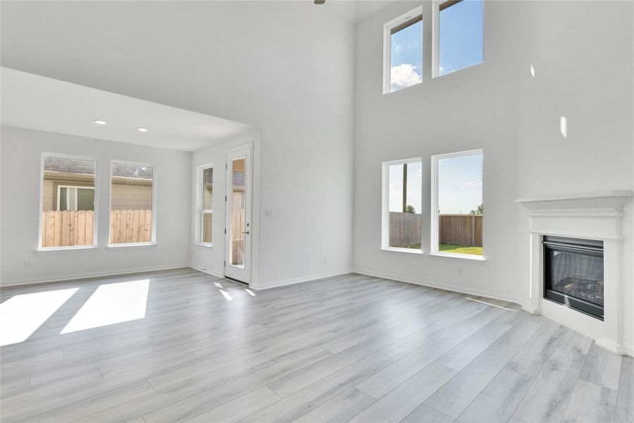 Unfurnished living room with a towering ceiling, a glass covered fireplace, and light wood finished floors Unfurnished living room with a towering ceiling, a glass covered fireplace, and light wood finished floors