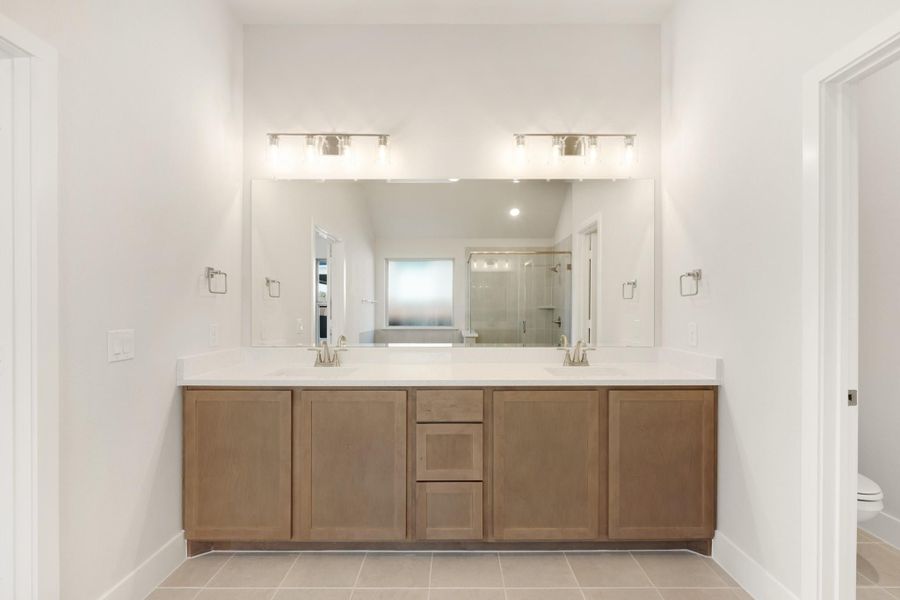 Bathroom with double-sink vanity, wood cabinets, white countertop, and large mirror with wall lighting Bathroom with double-sink vanity, wood cabinets, white countertop, and large mirror with wall lighting
