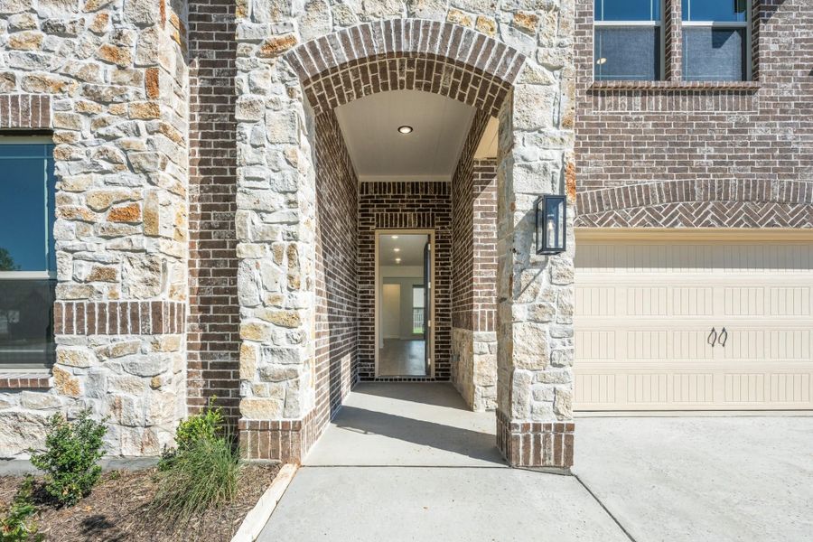 Home entrance with arched brick and stone surround, covered entryway, and two-car garage door visible to the right.