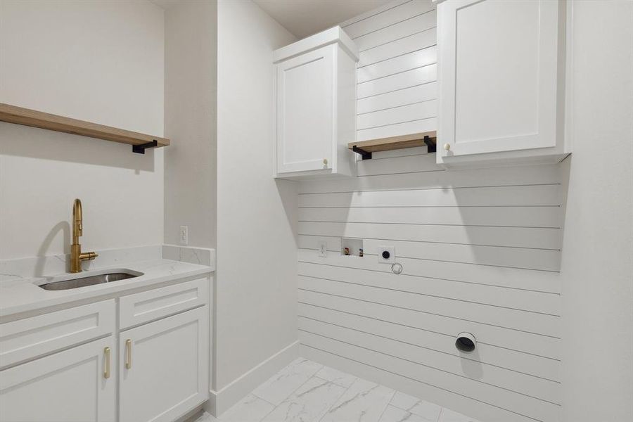 Clothes washing area with a sink, washer hookup, hookup for an electric dryer, marble finish floor, and cabinet space