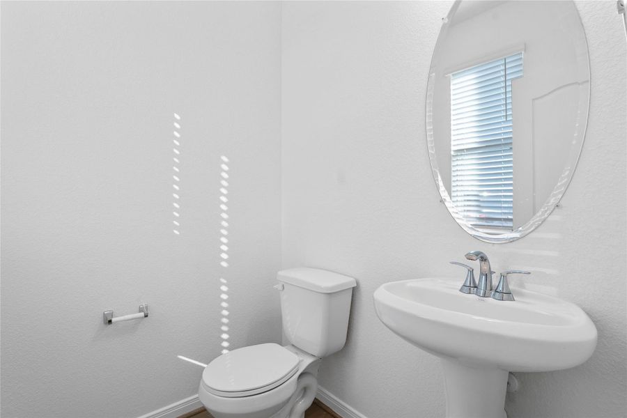 This main-level half bath features a pedestal vanity, oval mirror, window with privacy blinds, modern fixtures, and vinyl plank flooring. This main-level half bath features a pedestal vanity, oval mirror, window with privacy blinds, modern fixtures, and vinyl plank flooring.