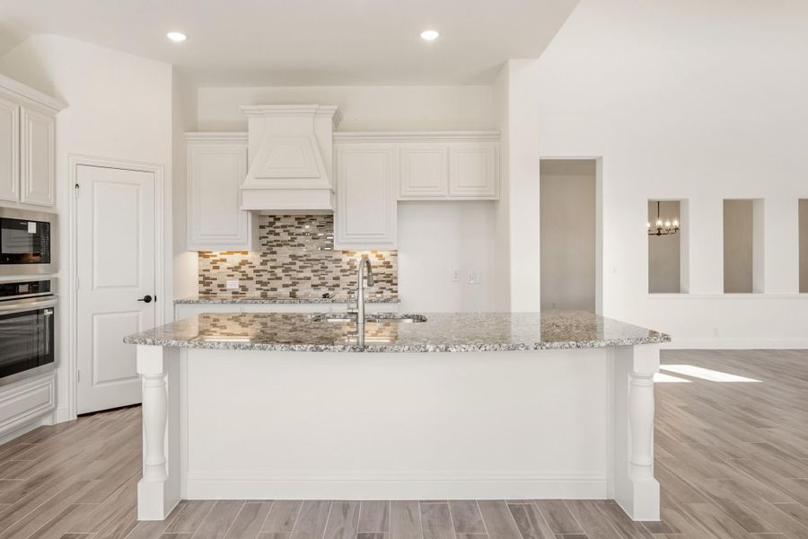 Kitchen with large granite island, white cabinets, tile backsplash, and wood-look floors Kitchen with large granite island, white cabinets, tile backsplash, and wood-look floors