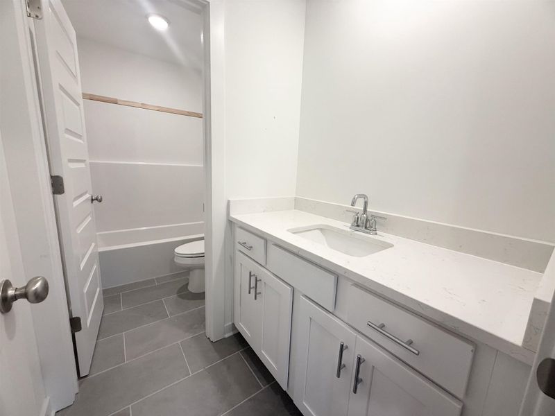 Full bath with vanity, dark tile patterned flooring, and washtub / shower combination