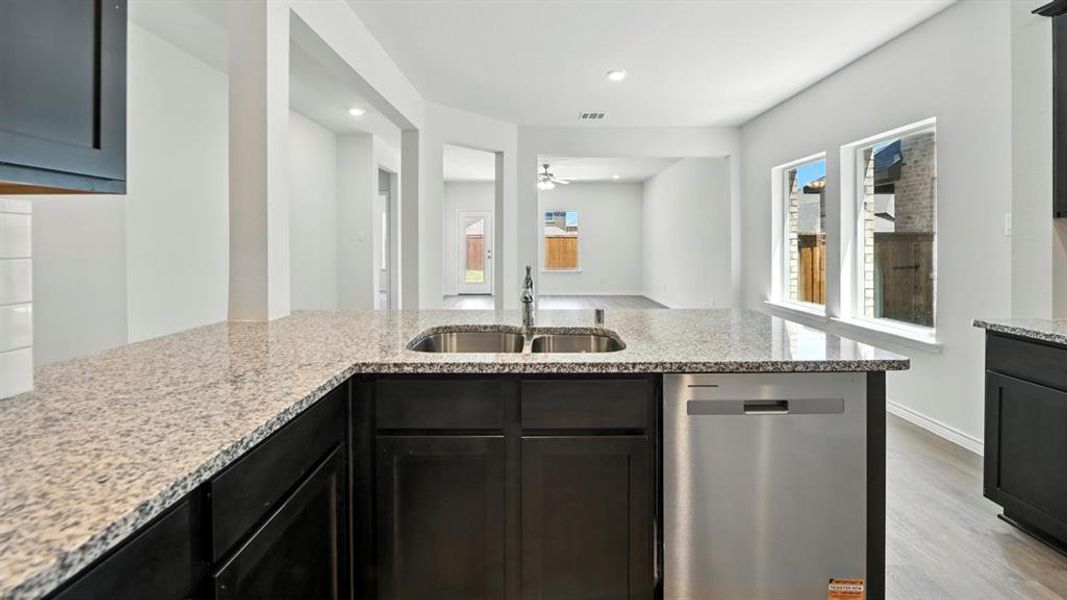 Kitchen with light stone countertops, dishwasher, light wood-type flooring, ceiling fan, and dark cabinetry