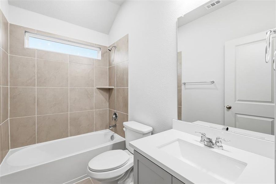Bathroom featuring bathtub / shower combination, vanity, a textured wall, and vaulted ceiling