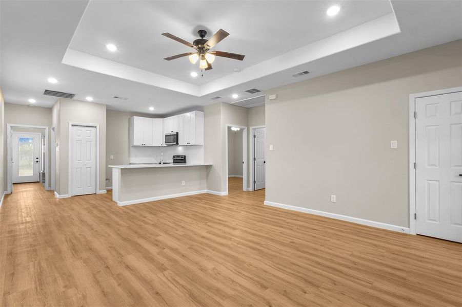 Unfurnished living room featuring recessed lighting, a raised ceiling, a ceiling fan, and light wood-type flooring