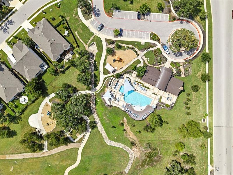 An aerial perspective showcases a manicured community space featuring a pool, playground, and paved pathways.