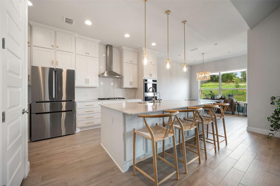 Kitchen with freestanding refrigerator, a center island with sink, white cabinets, light wood-type flooring, and recessed lighting