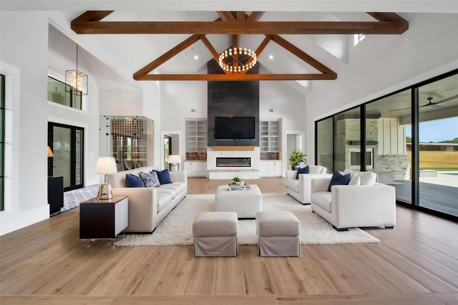 23' high ceilings with decorative wooden beams, a modern electric fireplace, and large sliding glass doors that open to a view of the majestic backyard resort oasis, creating a bright and inviting atmosphere. Curatively designed cabinets frame the black slate thats adds to the main focal point in this robost and stately gathering space.