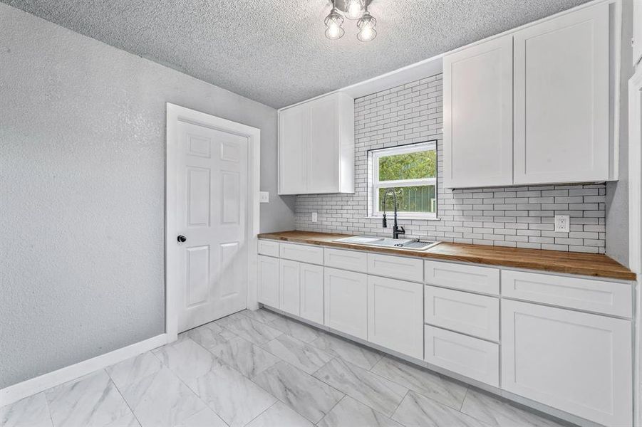 Kitchen with wooden counters, backsplash, white cabinets, a textured wall, and a textured ceiling Kitchen with wooden counters, backsplash, white cabinets, a textured wall, and a textured ceiling