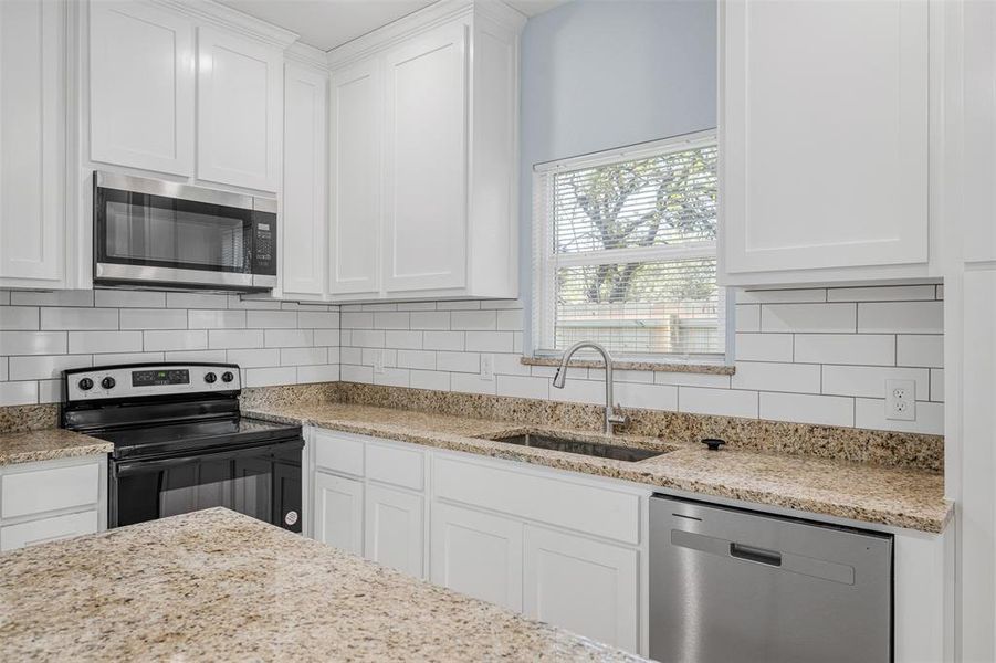 Kitchen with decorative backsplash, sink, white cabinets, and stainless steel appliances