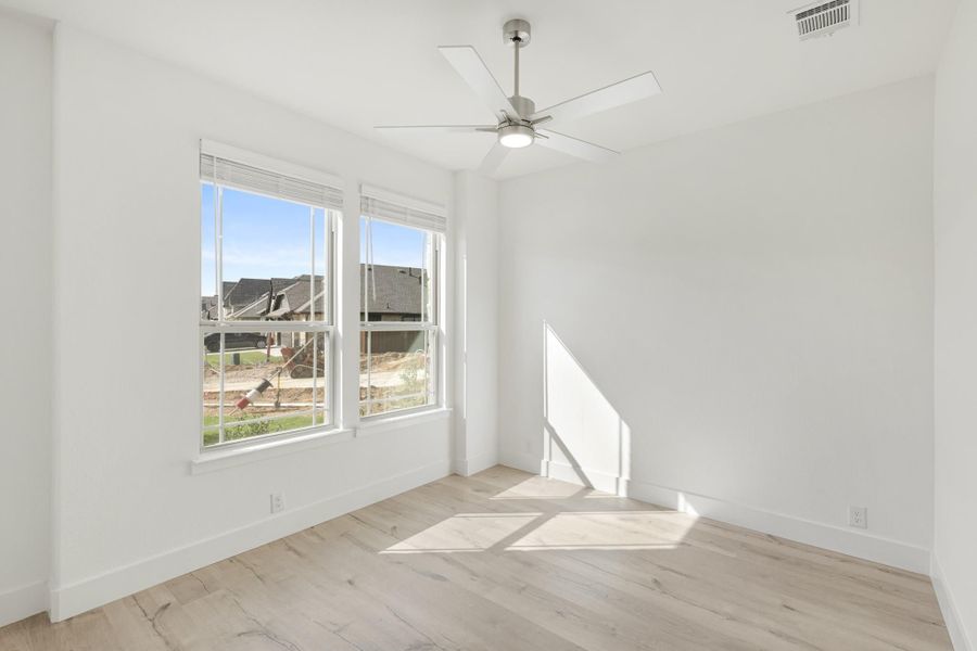 Empty bedroom with light wood floors, ceiling fan, and two windows with natural light