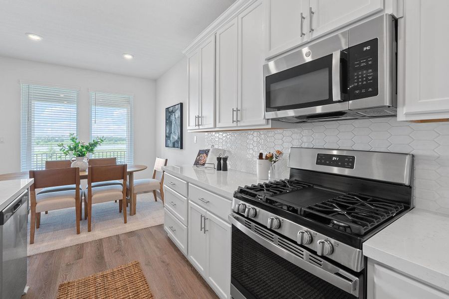 Kitchen featuring stainless steel appliances, light wood finished floors, light countertops, white cabinets, and tasteful backsplash