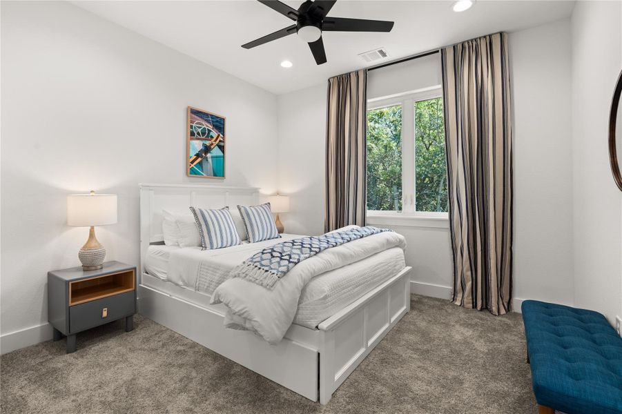 This bedroom features a modern ceiling fan, soft carpeting and beautiful views from the window.
