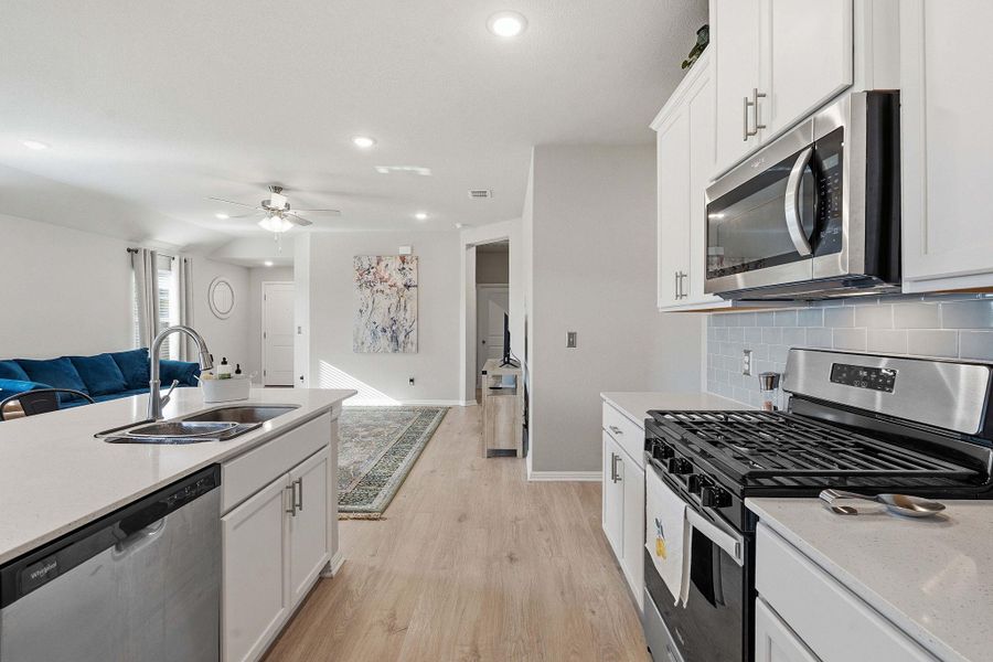 Kitchen with stainless steel appliances, open floor plan, white cabinets, light wood-style flooring, and light stone countertops Kitchen with stainless steel appliances, open floor plan, white cabinets, light wood-style flooring, and light stone countertops