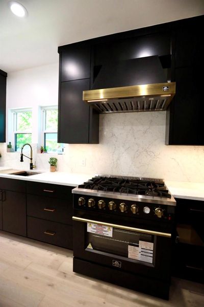 Kitchen with dark cabinets, high end black range oven, backsplash, light wood-style floors, and recessed lighting