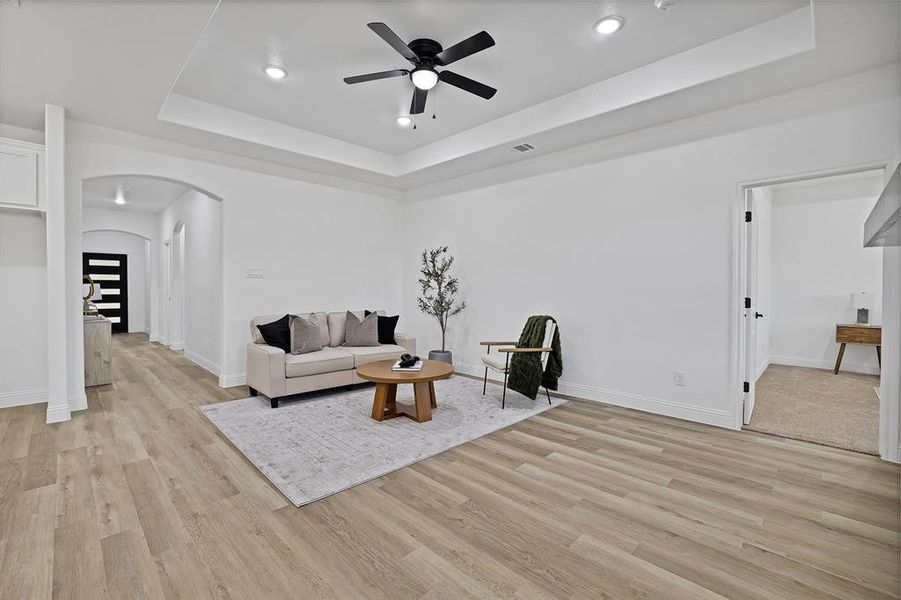 Living room featuring ceiling fan, light hardwood / wood-style floors, and a tray ceiling