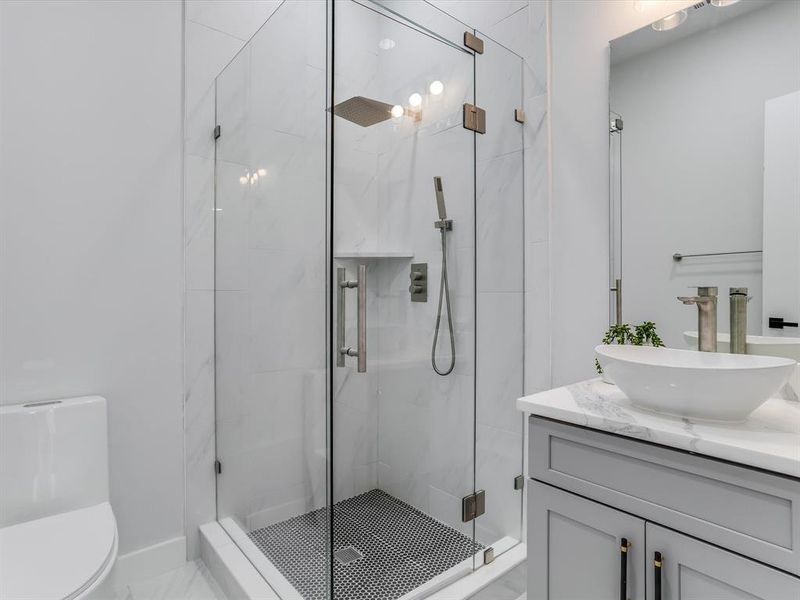 Downstairs guest bathroom featuring a glass-enclosed shower with black penny tile flooring, a built-in shower niche, and a rain shower head Downstairs guest bathroom featuring a glass-enclosed shower with black penny tile flooring, a built-in shower niche, and a rain shower head
