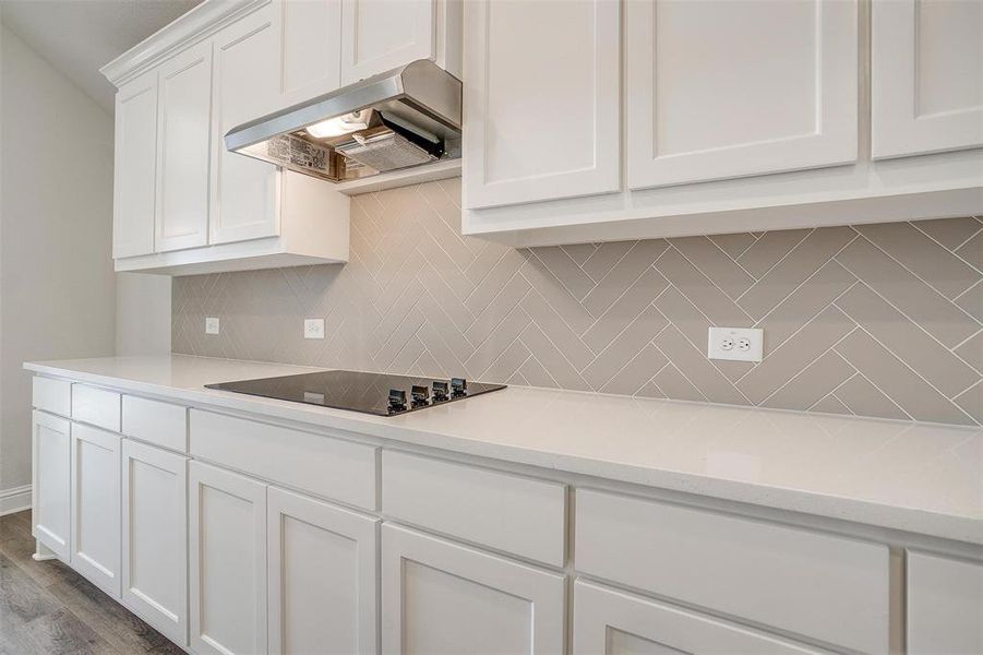 Kitchen featuring island exhaust hood, black electric stovetop, light wood-type flooring, backsplash, and white cabinetry