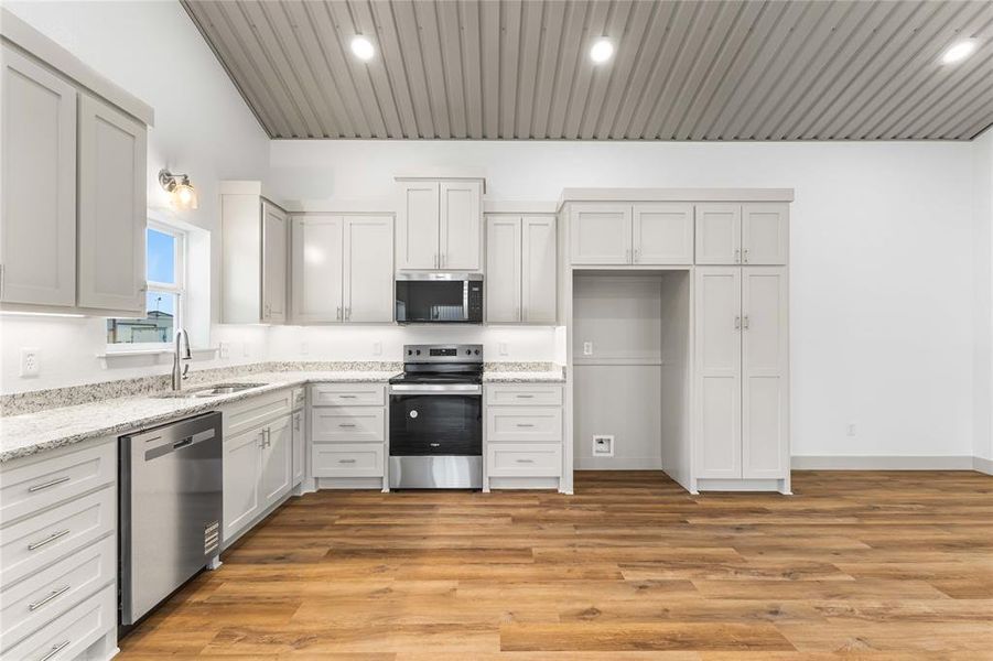 Kitchen with stainless steel appliances, a sink, light stone counters, lofted ceiling, and light wood-style floors Kitchen with stainless steel appliances, a sink, light stone counters, lofted ceiling, and light wood-style floors
