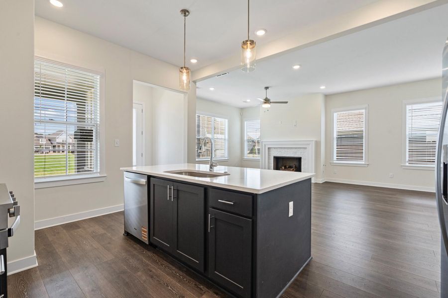 Spacious kitchen island with a built-in sink, stainless steel dishwasher, and dark cabinetry, complemented by overhead pendant lighting Spacious kitchen island with a built-in sink, stainless steel dishwasher, and dark cabinetry, complemented by overhead pendant lighting