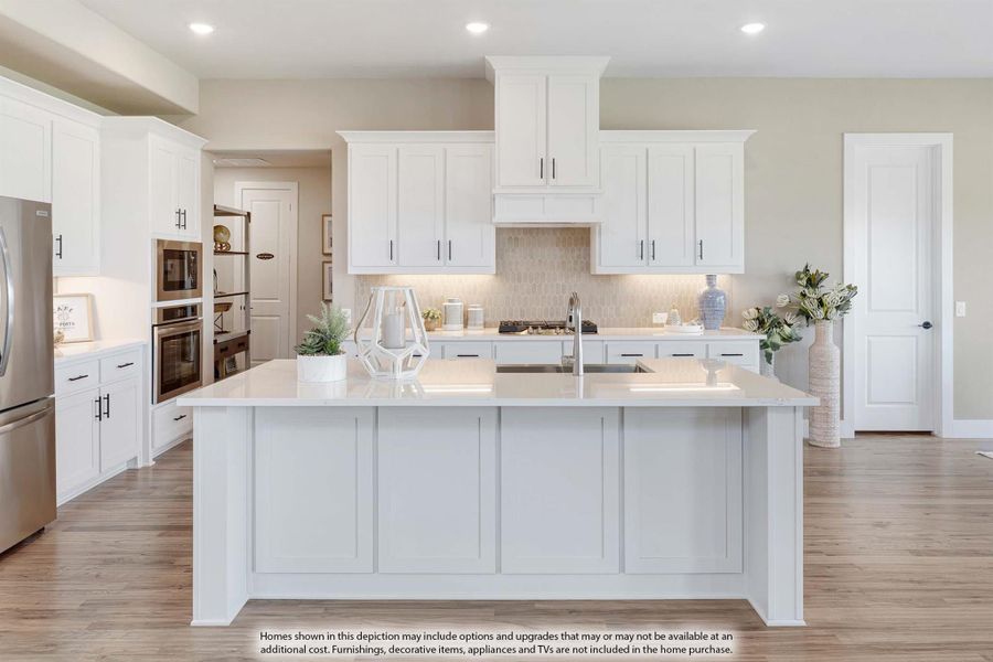 Kitchen with large center island, white cabinets, quartz countertops, and stainless steel appliances on light wood floors.