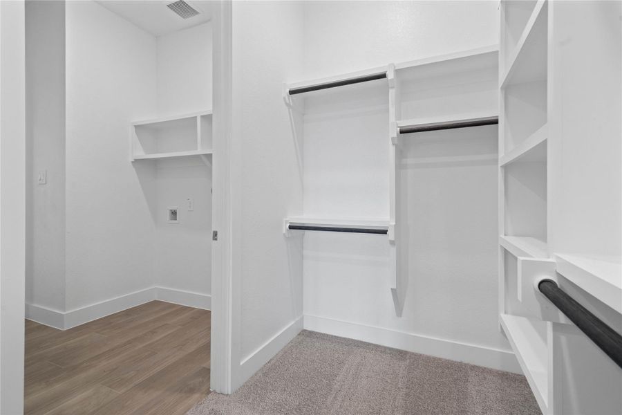 The spacious walk-in closet is equipped with clean white shelving and sturdy matte black hanging rods, offering extensive solutions for organizing an entire wardrobe. This closet also features direct access to the laundry room, a dream feature for modern living.
